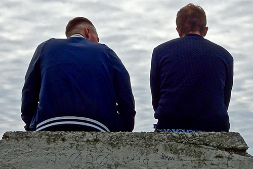 Generic image of the backs of two young men sat on a stone