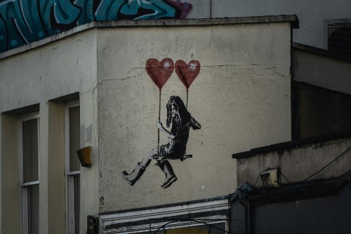 Image shows graffiti image of a female sat on a swing upheld by heart balloons.