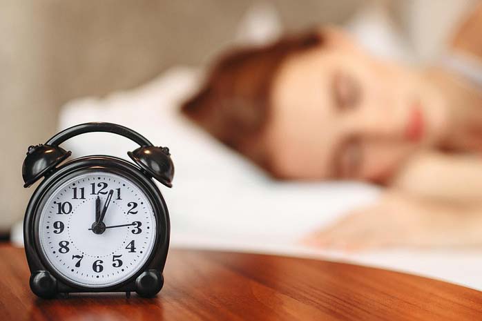 A women sleeping with an alarm clock on a bedside table