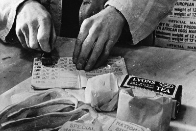 Civilian rationing: A shopkeeper cancels the coupons in a woman's ration book in 1943.