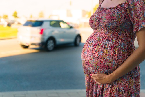 Generic image of a pregnant woman stood by road with polluting cars