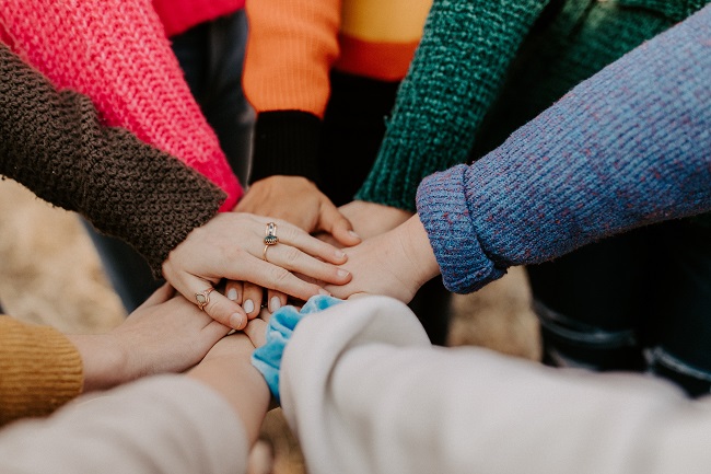 Circle of women placing hands on each other's hands.