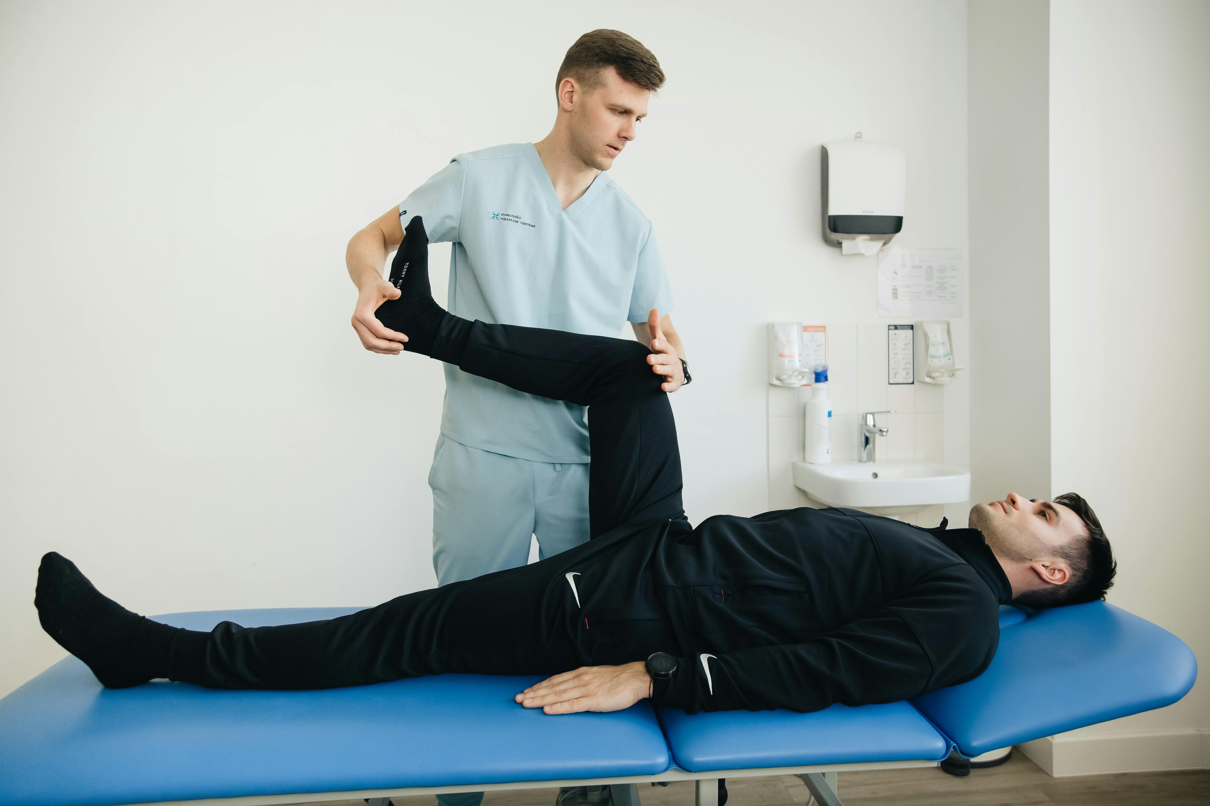 A health professional bends the knee of a prone patient in a clinical setting.