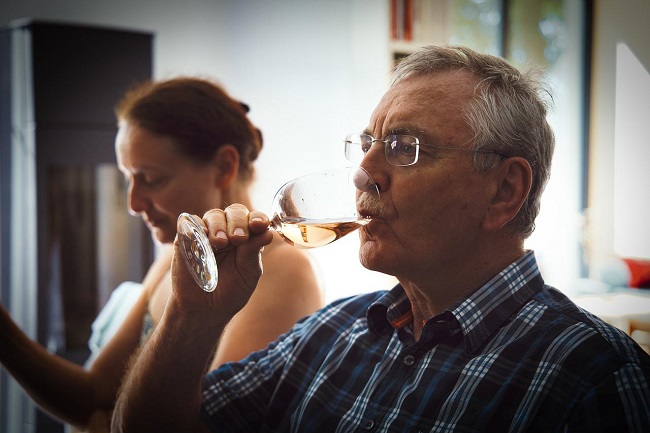 Man drinking a glass of wine in kitchen in the foreground with woman in the background