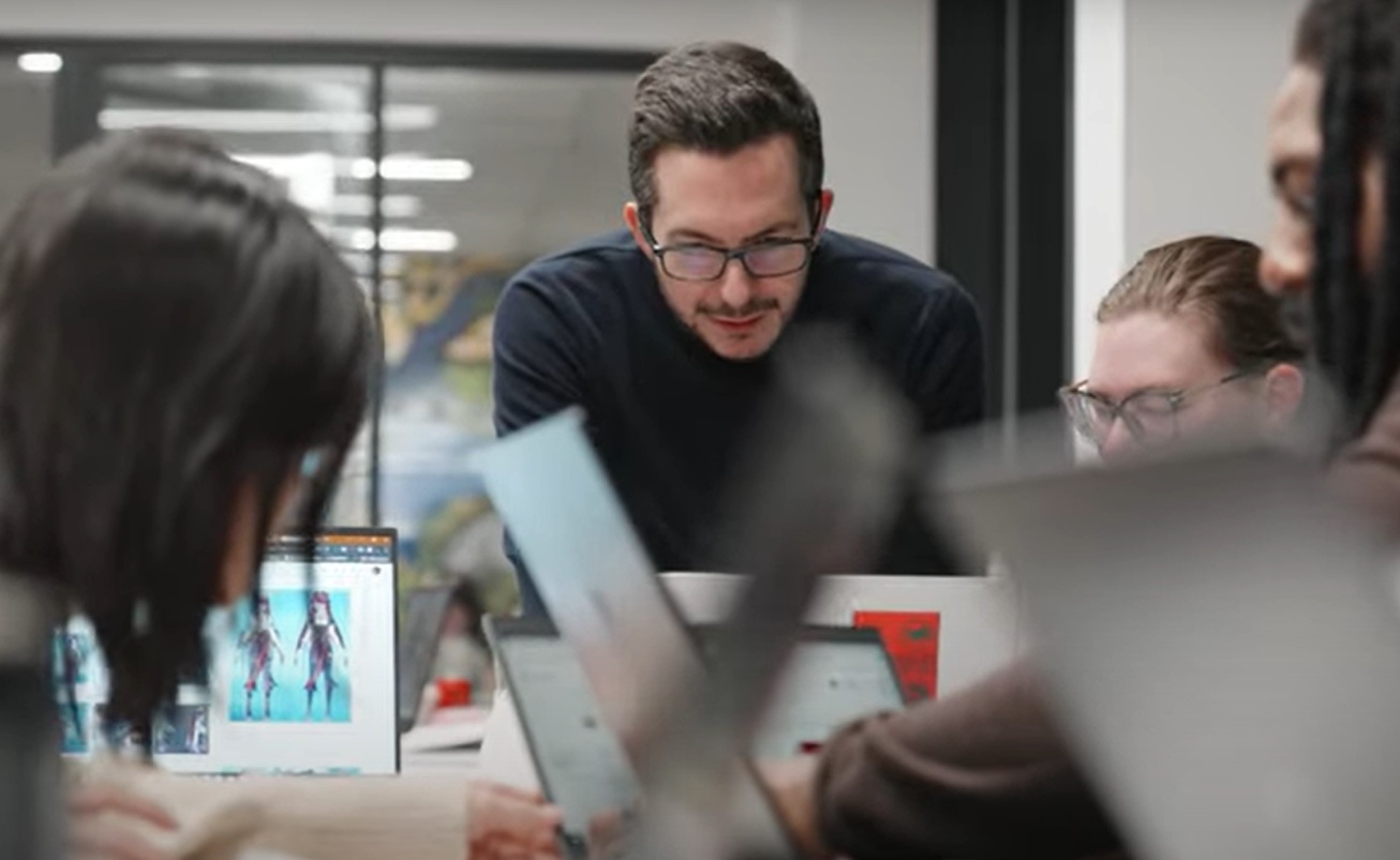 man stood at front of a table with a team of gamers on laptops