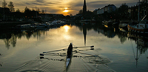 Team of 4 rowers rowing a racing boat on a river at sunrise. Image links to information about the Saltford Boat House.
