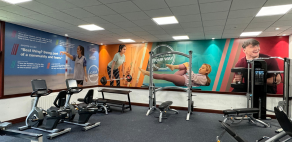 Gym area set up with weight machines and seated cycling machines with participant quotes and pictures displayed on the walls.