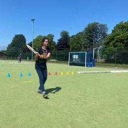 Arisha standing on a sports fields with a cricket bat in swing after hitting a ball