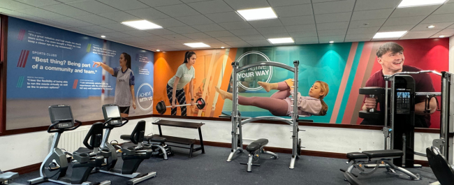 Gym area set up with weight machines and seated cycling machines with participant quotes and pictures displayed on the walls.