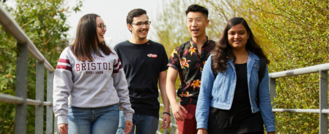 Four diverse students smiling and laughing together on a walk.