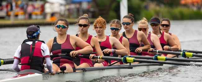 A rowing boat with a coxswain and 8 female rowers on the water moving.