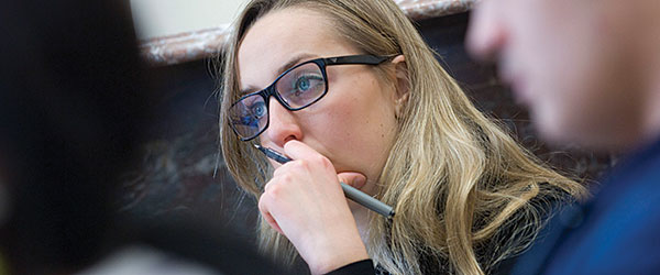 A white woman with blonde hair and glasses looking thoughtful.