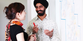 A woman and a man wearing a turban talking and smiling.