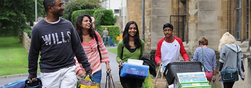 A group of students carrying boxes and luggage moving into accommodation.
