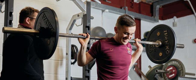 A student smiling while lifting weights in a gym