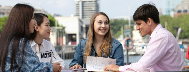 Four students sitting and talking by the harbour