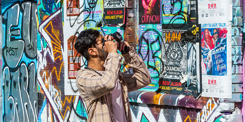 A male student taking a photo of a wall covered in posters and graffiti