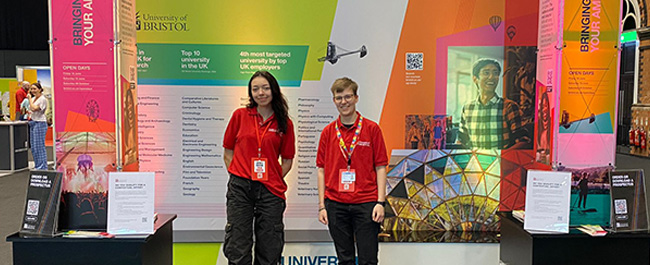 student ambassadors stood in front of a colourful University of Bristol stand at a UCAS fair