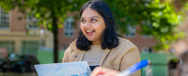 A student smiles while sitting in a square and working on her laptop