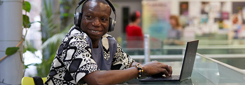 A smiling man working on a laptop with headphones on