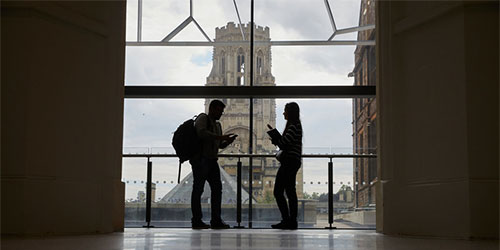 Silhouette of 2 students standing in front of a window in a University building. The Wills Memorial Building is in the background. 