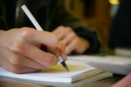 Hands holding a pen and writing on a notepad