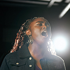 Profile shot of a student, Laura, who is singing with a spotlight shining behind them.