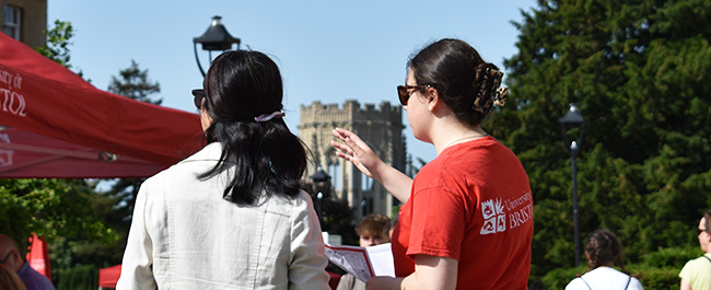 A student ambassador directing a guest at an open day with Wills memorial building in the background.