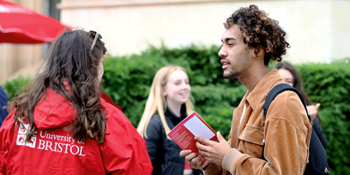 A student holding an open day guide and talking to a Bristol student ambassador who is wearing a red University of Bristol jacket. 