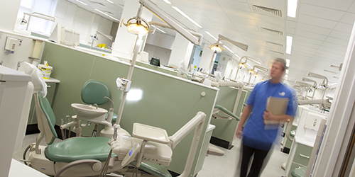 A person walks through a large room containing a number of dental chairs. 