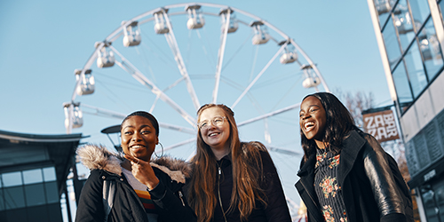 Three students laughing while walking through Millennium Square in Bristol. 