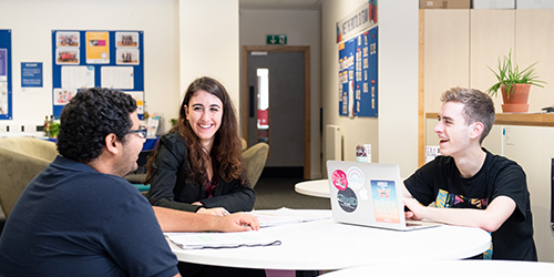 Three students sat around a table smiling. 