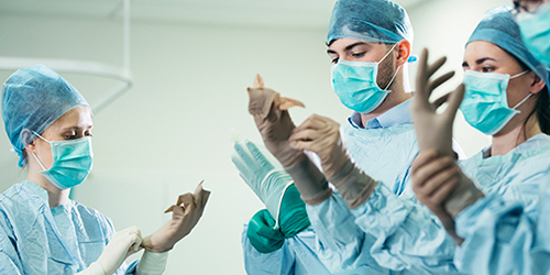 Students in surgical masks, caps and scrubs pull on their gloves