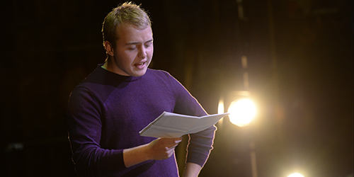 A performer reads from a script on stage.