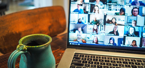 Laptop with video conference on-screen and a mug on the left.
