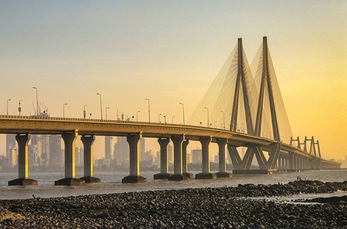 A huge road bridge crossing the sea towards the yellow sunrise.