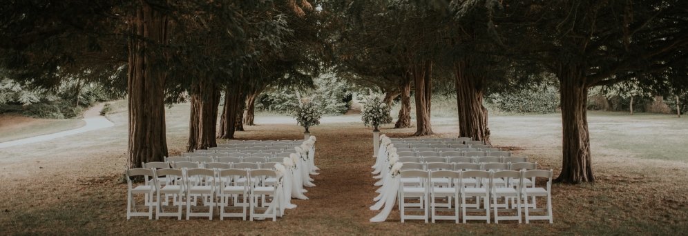 The lawns of Goldney House setup for a wedding ceremony with rows of white chairs between the yew tree avenue. 