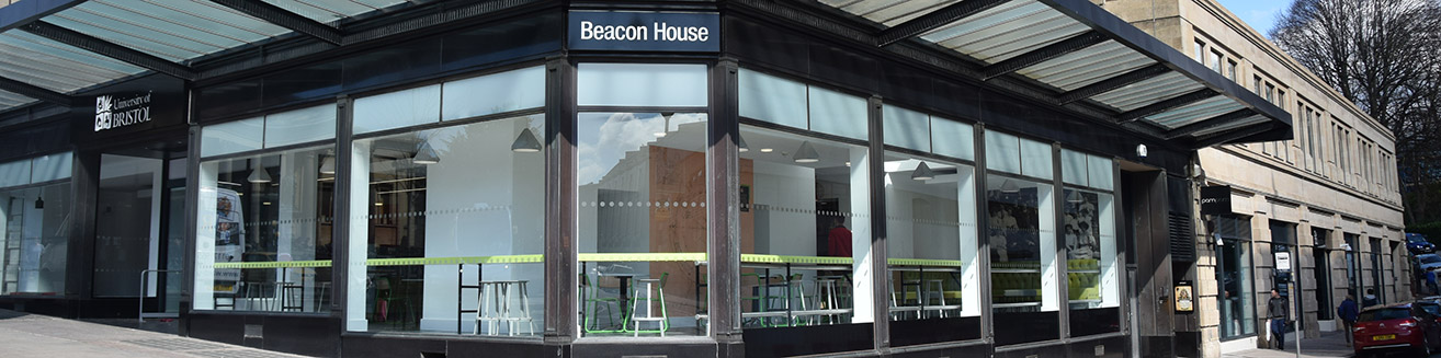 View of Beacon House from the corner of Queens Road and Queens avenue, showing the entrance to the building and some seating through the glass windows.